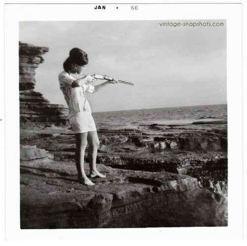 Vintage photo of a 1960s young woman shooting a gun at ocean