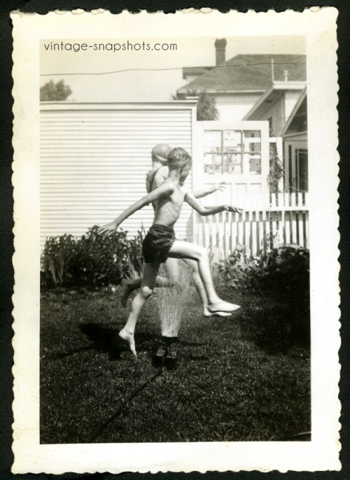 Vintage photo of a young boy and girl leaping over a sprinkler