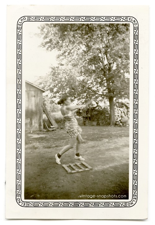 Vintage Elko-border photo of a woman swinging a baseball bat while standing at a home-made home plate
