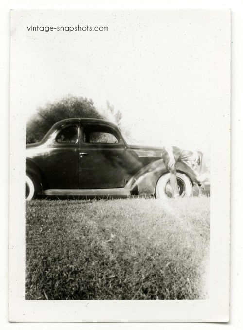Vintage snapshot with odd light leak/mistake obscuring man sitting on car