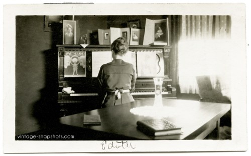 Vintage photo of woman named Edith playing the piano with sheet music and family photos on the instrument