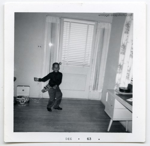 1963 vintage snapshot photograph of black boy dancing to record player while wearing toy gun